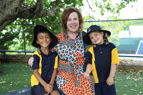 Adult standing outdoors with two students in school uniform.