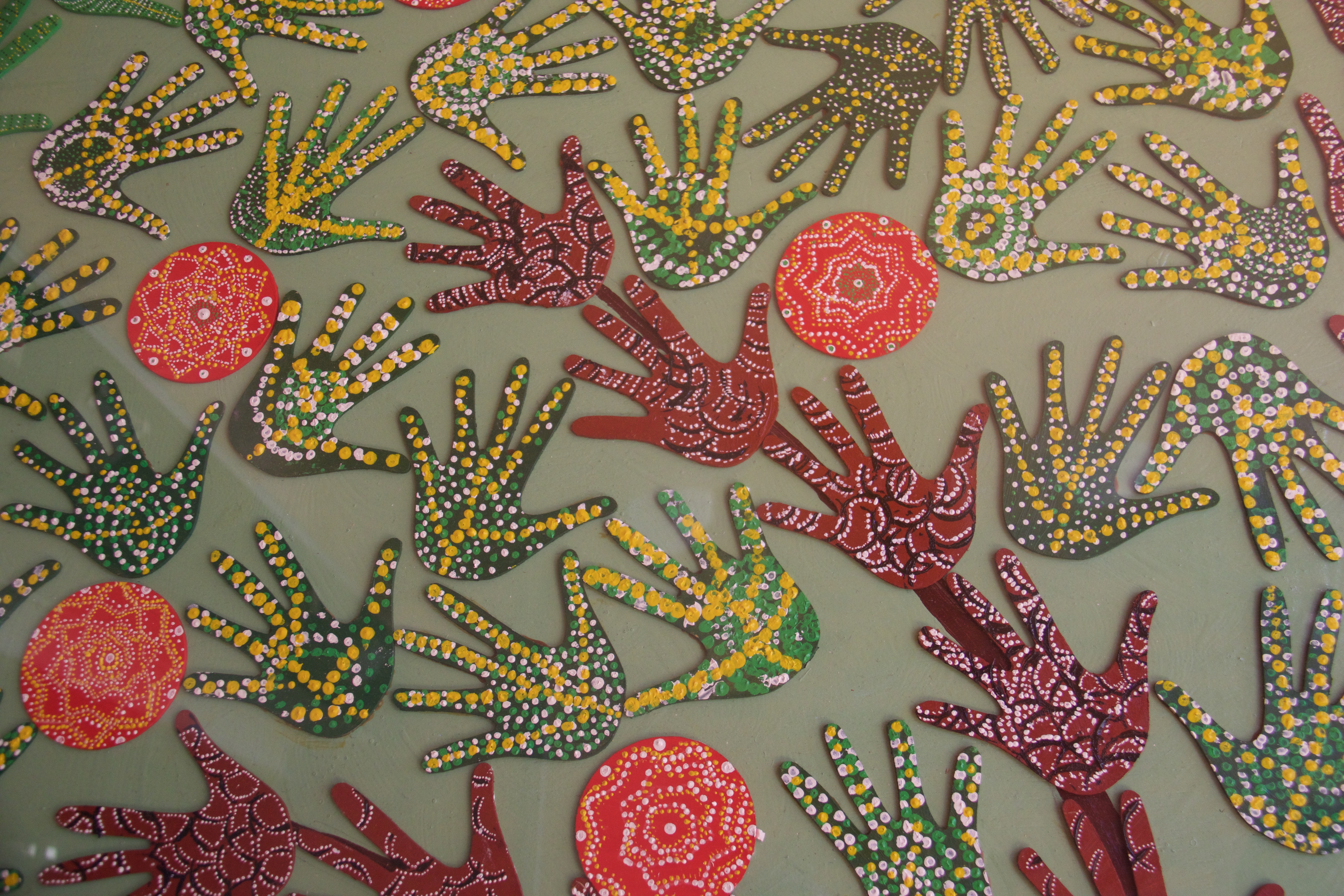 Artwork featuring painted handprints and circular dot patterns in red, green, yellow, and white.