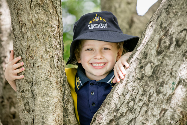 Student in school uniform outdoors among trees.
