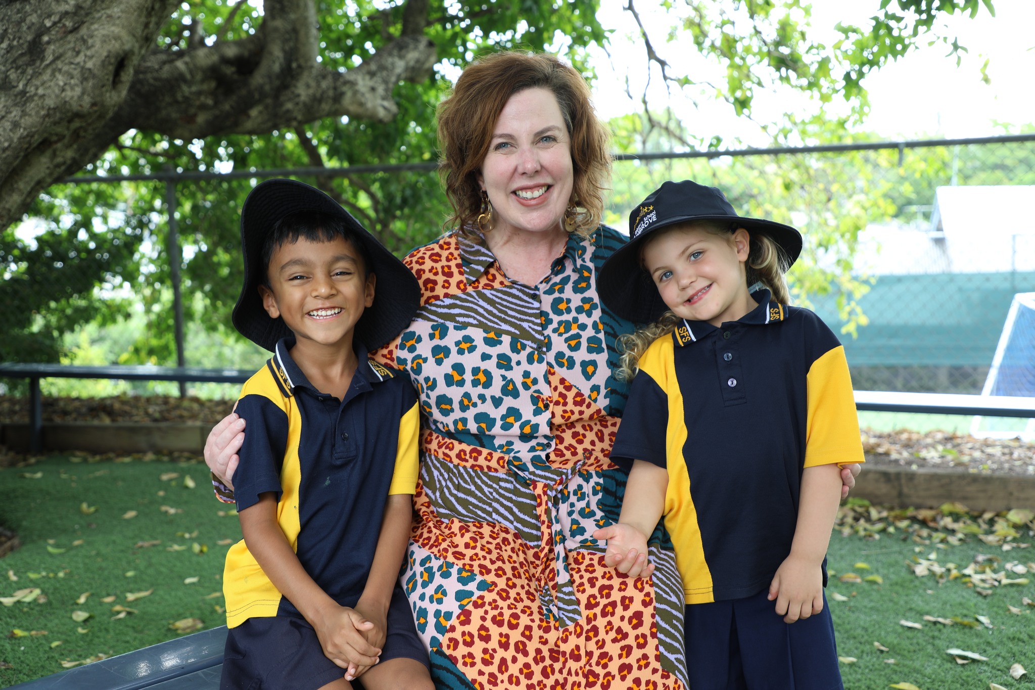 Adult standing outdoors with two students in school uniform.
