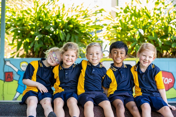 Group of students in school uniform sitting together in an outdoor play area.