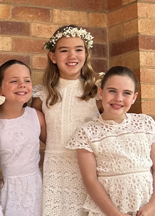 Three students dressed in white standing together against a brick wall.