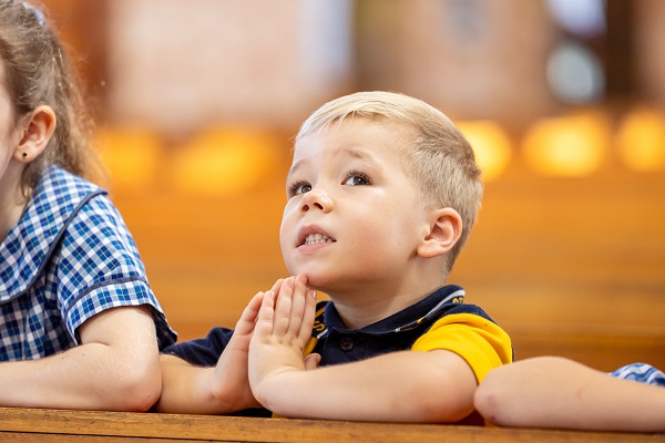 Student seated in a church pew with hands together during a religious activity.