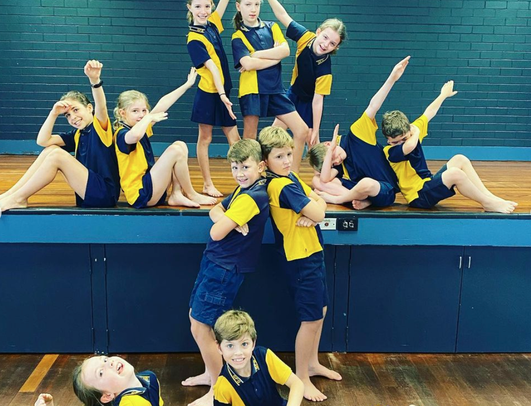 Students in school uniform posing together on a stage during a creative movement or drama activity.