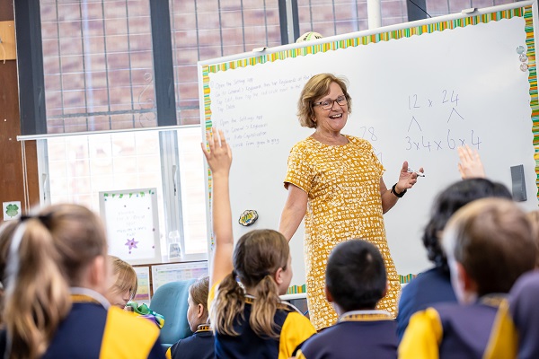 Classroom lesson with students raising their hands to participate.