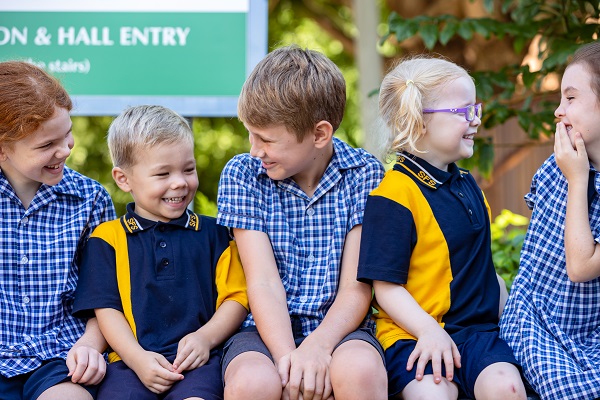 Students in school uniform sitting on a bench outdoors together on school grounds.